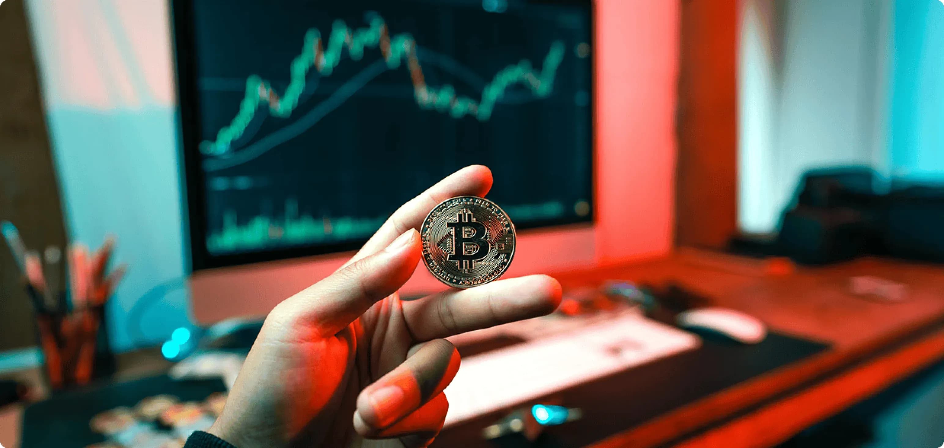 Financial Services — hand holding a Bitcoin token in front of trading screens